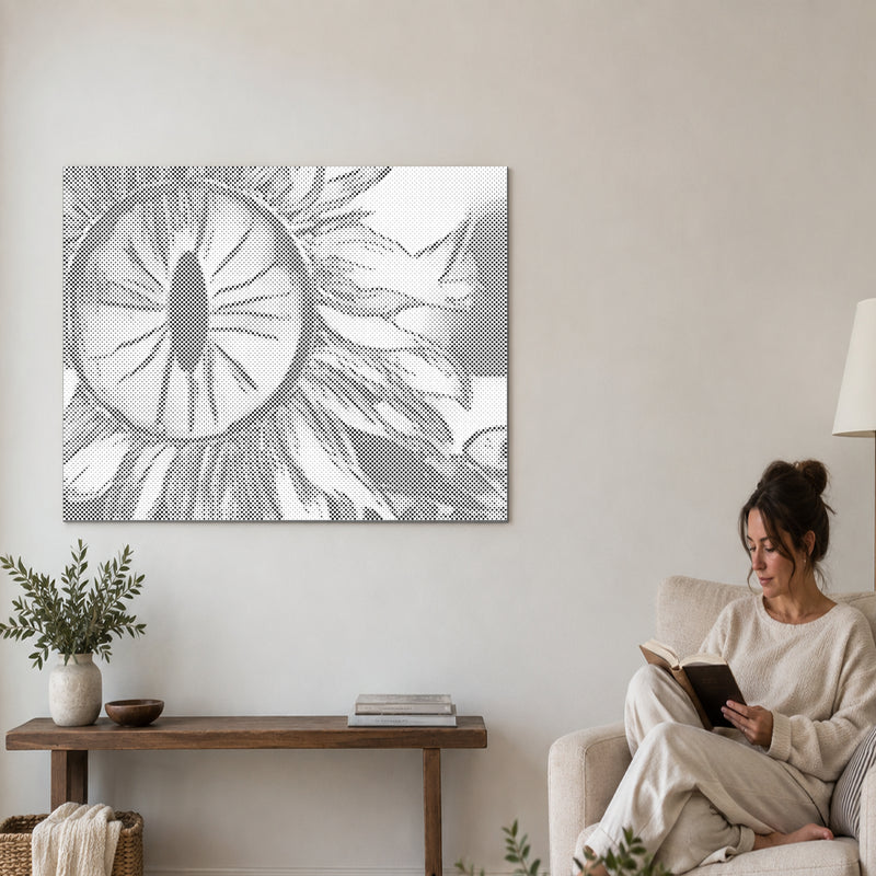 Punktmalerei-Leinwand “Sonnenblumenauge”, an einer Wohnzimmerwand, daneben liest eine Person in einem Sessel.